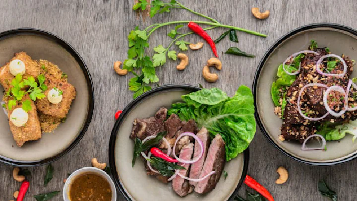 A rustic wooden table displays a meal with roasted meats, rice, and various dishes.