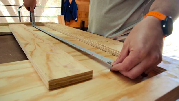 A person uses a ruler to measure a plank of light-colored wood.