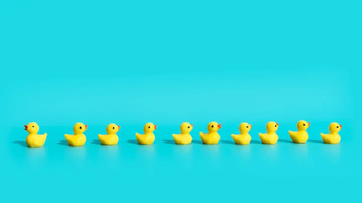A row of bright yellow, stylized rubber ducks arranged horizontally against a solid turquoise background.