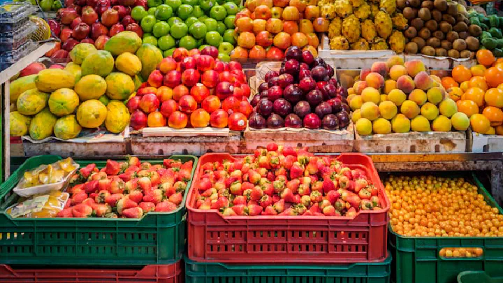 Vibrant market stall overflowing with brightly colored piles of fresh fruits and vegetables, including apples, tomatoes, and mangoes.
