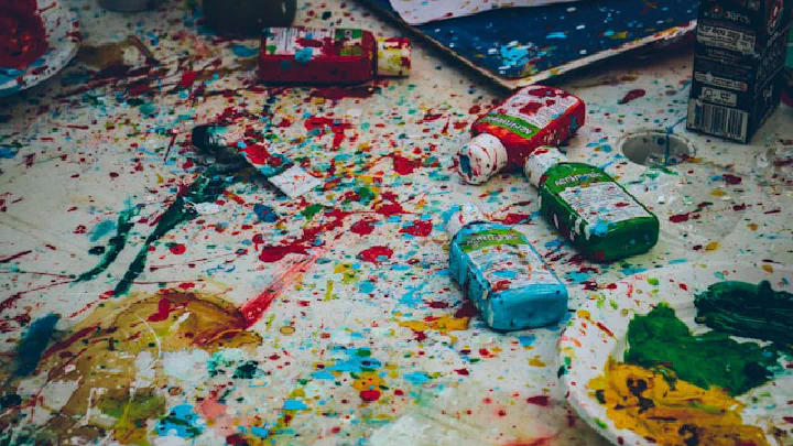 A splatter of paint and paint supplies covers a white surface.