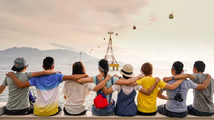 Group of people standing on a pier overlooking the sea, with a large Ferris wheel structure visible in the background.