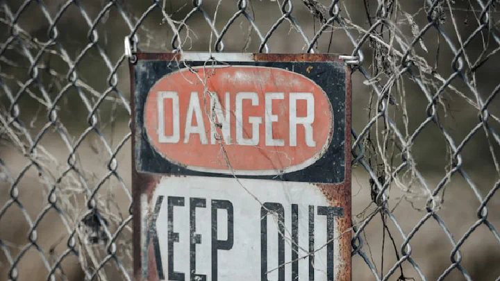 A weathered, rusty warning sign reading "DANGER KEEP OUT" hangs on a chain-link fence.