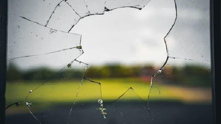 Shattered glass frames a blurry, overcast outdoor landscape.