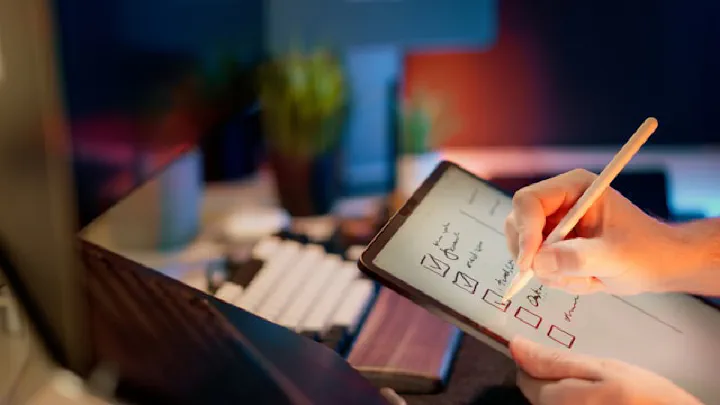 A hand uses a pencil to mark a detailed checklist on a clipboard, resting on a desk.
