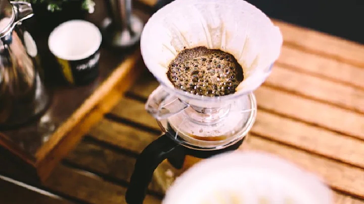 Pour-over coffee dripper filled with grounds rests on a slatted wooden surface.